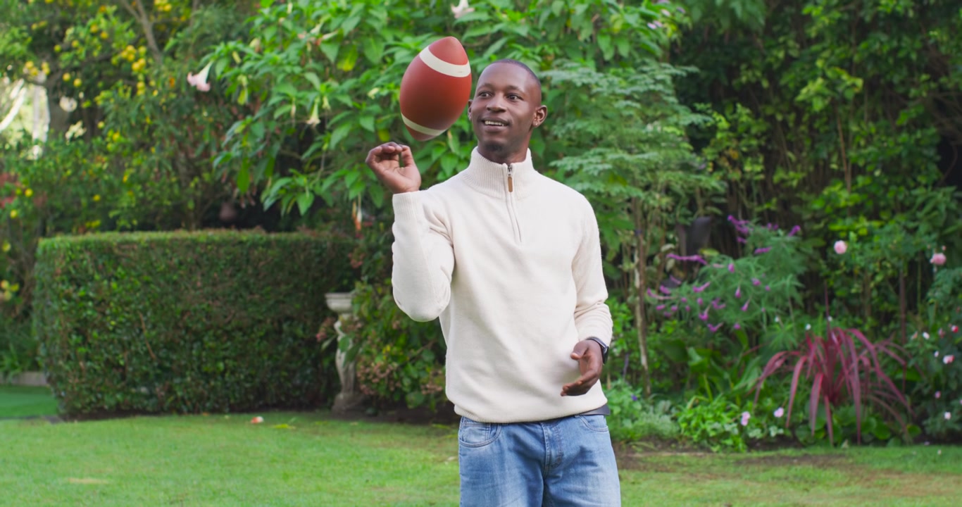 African American adult male shifting grip, tossing and catching football in yard practicing catches