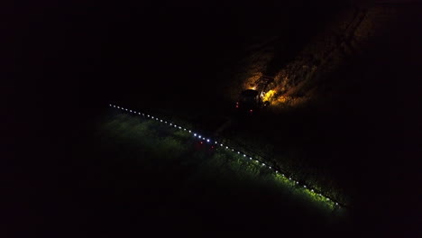 tractor con remolque y brazo metálico ancho con boquillas rociando pesticidas sobre el campo verde en la oscuridad de la noche