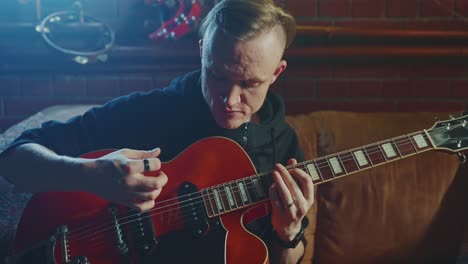 man playing a red electric guitar at home