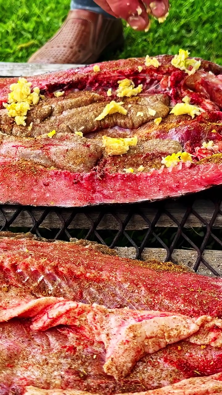 Hand seasoning fresh fish fillets outside, preparing for grilling.