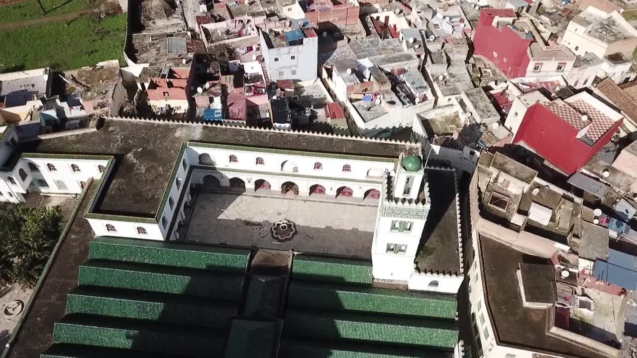 Scatto dettagliato con drone che cattura l'architettura interna della Masjid al-Aazam. Evidenzia gli archi tradizionali marocchini, il minareto bianco e i tetti verdi simmetrici nel cuore di Larache