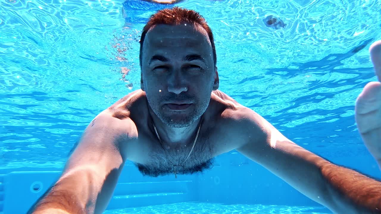 Man swimming underwater. Healthy man diving in the swimming pool and looking at camera. Happy male showing ok sign inside the pool.