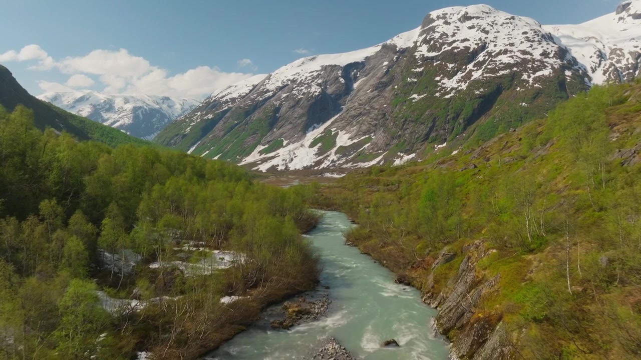 Un drone cinematografico sorvola un fiume glaciale in un paesaggio spettacolare con montagne innevate e un ghiacciaio sotto cieli estivi azzurri e limpidi. Scena epica di natura alpina e di viaggio. Austerdalsbreen, Norvegia