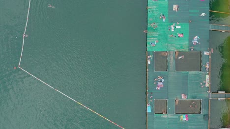 Tourists-sunbathing-on-pontoon-floating-pier-and-swimming-in-lake,-top-down-view