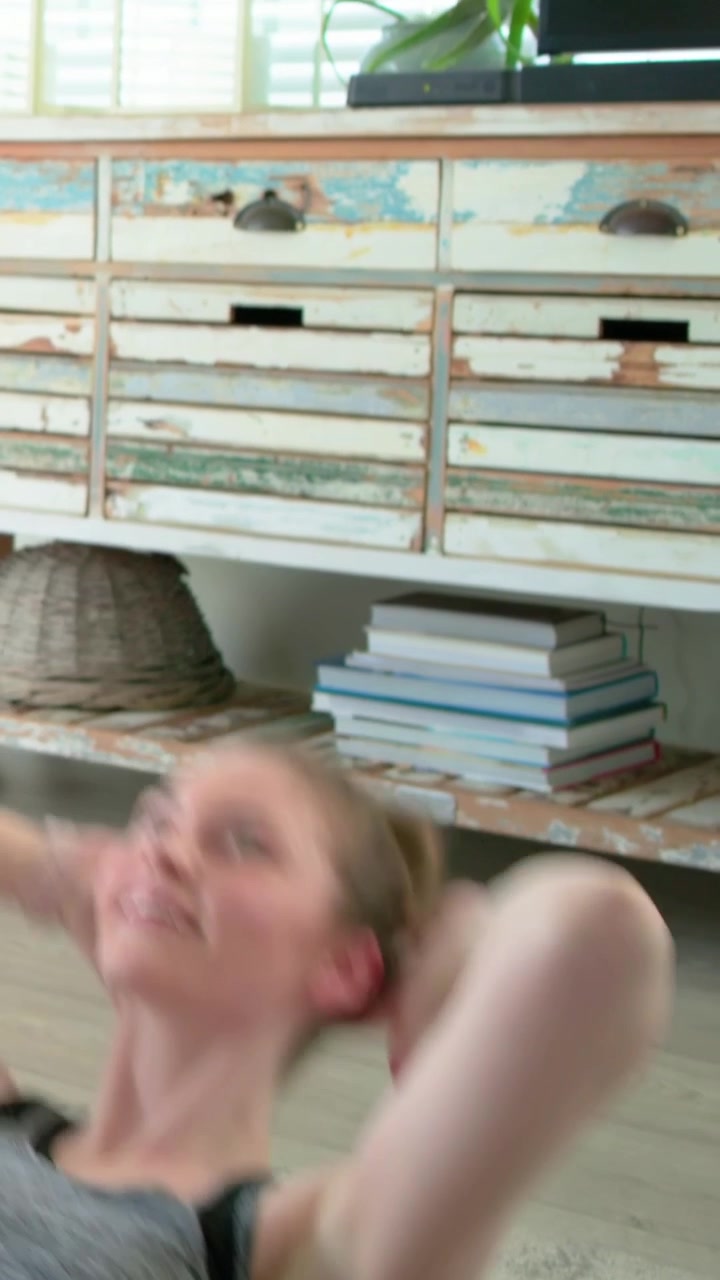 Vertikales Video: Frau beginnt gestützt Crunches zu Hause auf einer Matte für die Rumpfmuskulatur, trägt graues Oberteil, mit Platz für Text.