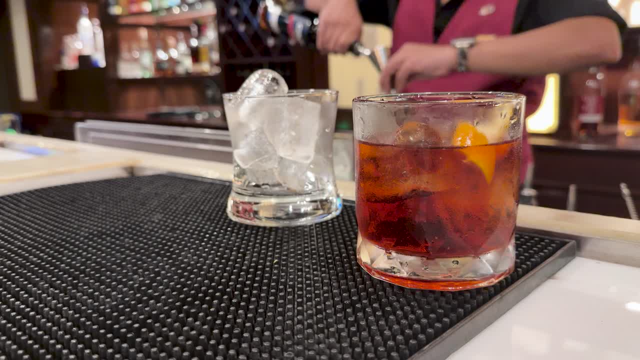 Bartender in uniform prepares classic cocktails on bar mat, warm lighting, shallow depth of field