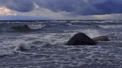 waves in the sea during a thunderstorm at sunset, large stones on the sea shore