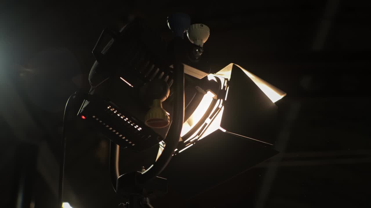 Halogen source of constant lighting equipment. Lightweight fresnel spotlight searchlight is on set during shooting of film. Lamphead. Dark stage, scene. Movie cinema production. Gafer's work on-set
