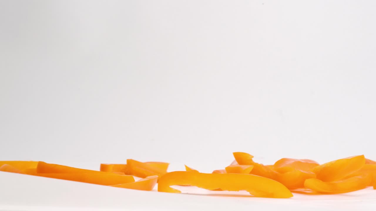 trozos de pimiento naranja en rodajas que caen sobre la mesa blanca y rebotan en un montón a cámara lenta