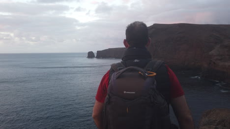 mature man with a backpack on his back walks along the cliffs of the coast of the municipality of galdar and where the pardido cliff can be seen