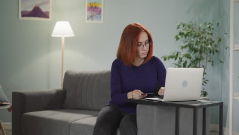 Red-haired-woman-in-glasses-enters-card-details-into-laptop