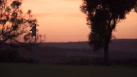 Establecimiento-De-Una-Vista-De-Una-Bandera-Ondeando-En-Medio-De-Una-Cancha-De-Golf-Durante-La-Hora-Dorada