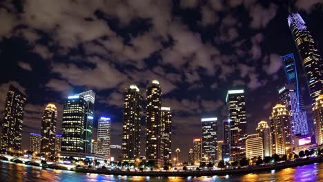 dramatic urban nightscape featuring luminous skyscrapers casting glimmering reflections across rippling water surface under moody clouded evening sky