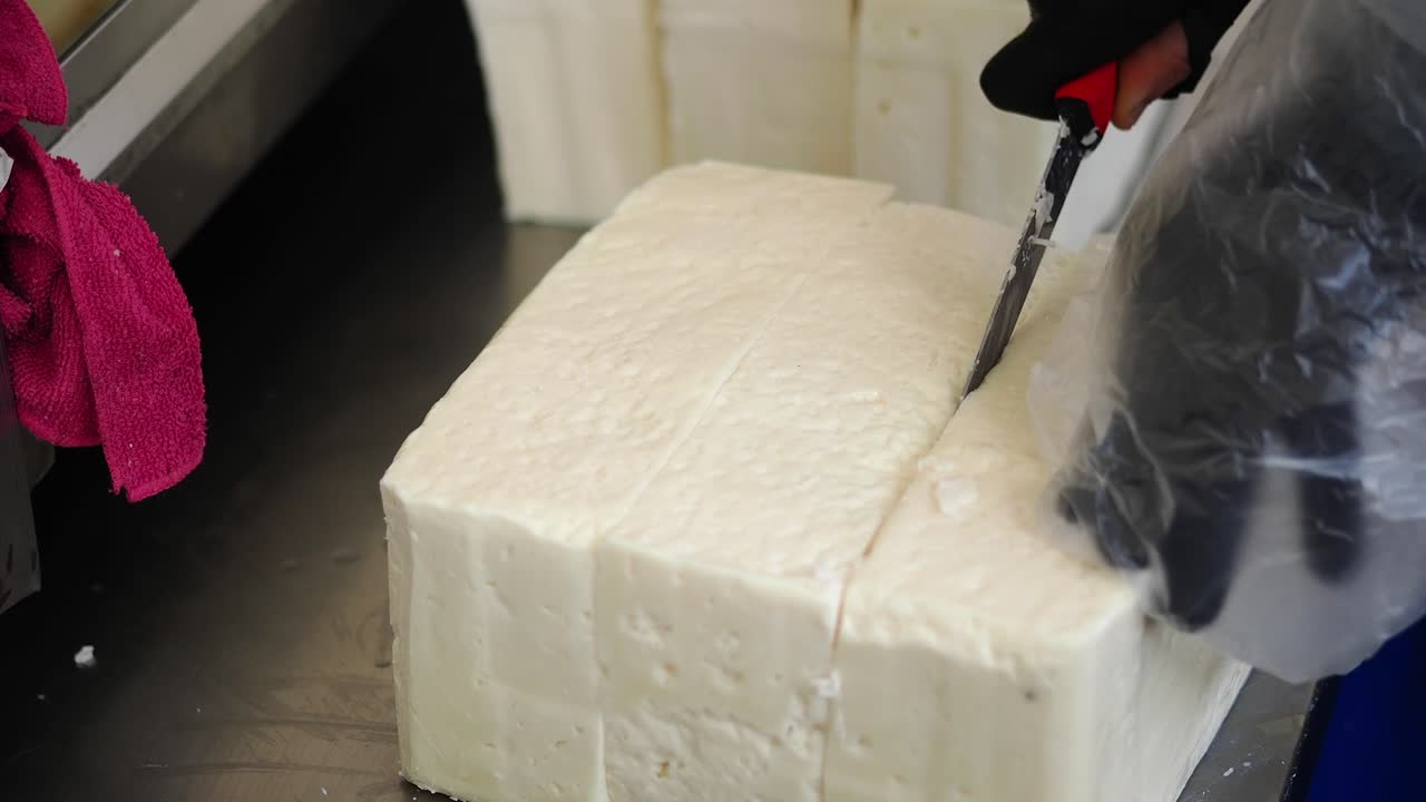 Close-up of Hands Cutting a Large Block of White Cheese