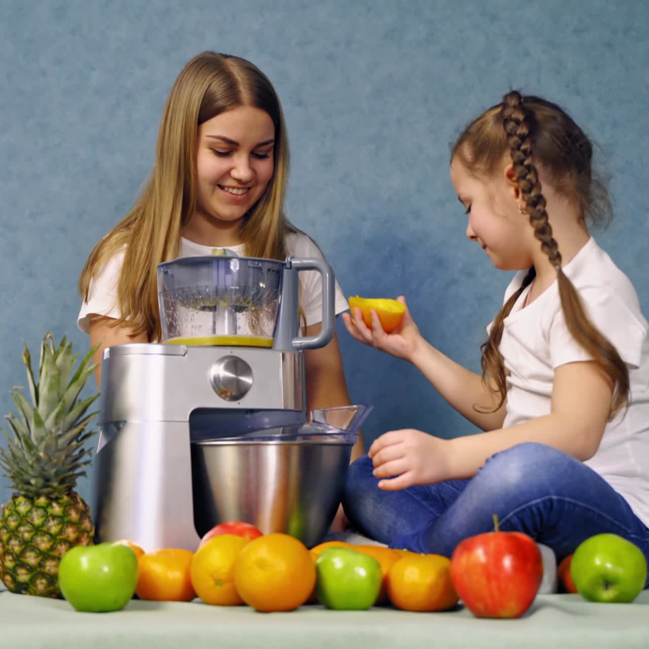 Mother and daughter making juice from fresh fruits. Little girl sitting on the table and tasting sour orange. Healthy vitamins in ripe fruits.