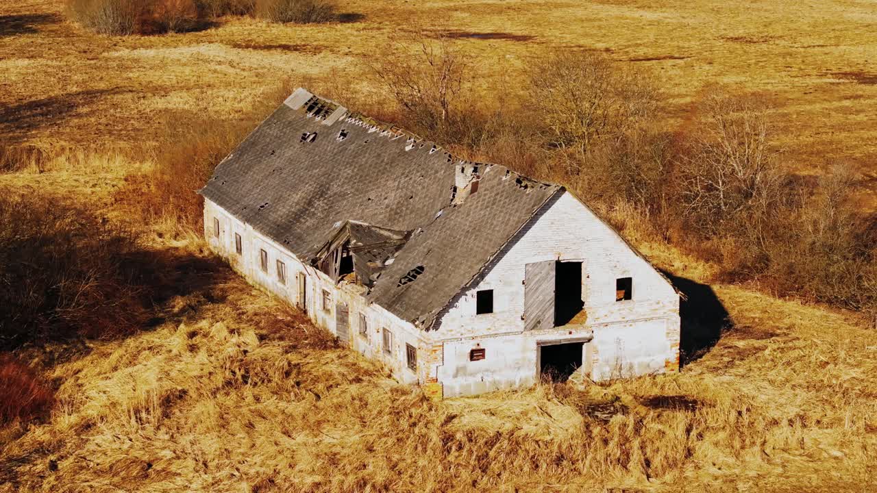Abandoned white-brick farm building with collapsed roof, aerial, rural Latvia