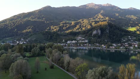 Una-Vista-Aérea-De-Weesen-Y-Walensee-Muestra-Un-Pequeño-Puerto-Deportivo,-Una-Zona-Residencial-Y-Una-Majestuosa-Montaña-Bajo-El-Sol.