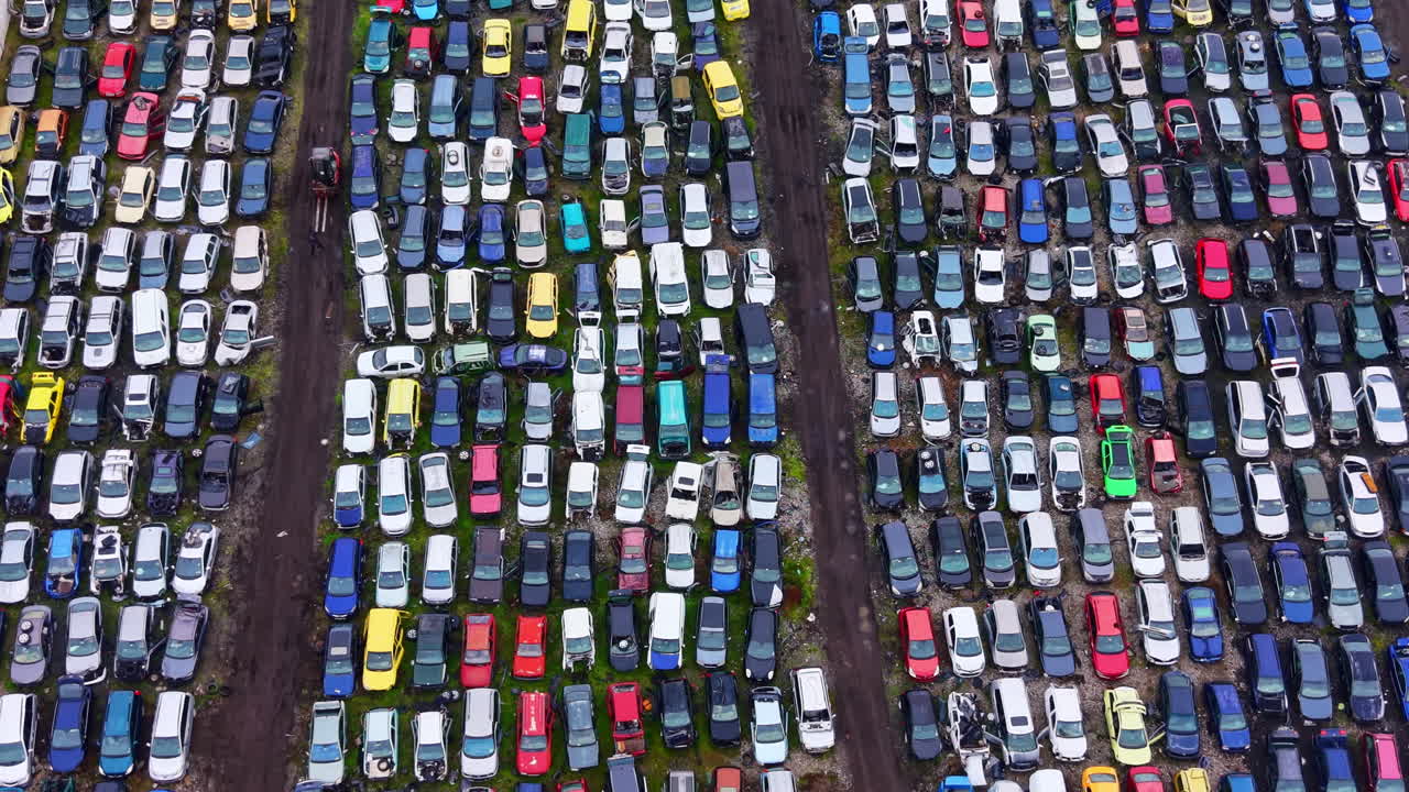 Mange biler parkeret sammen på et stort område på en losseplads i dagslys med klare farver og forskellige synlige modeller