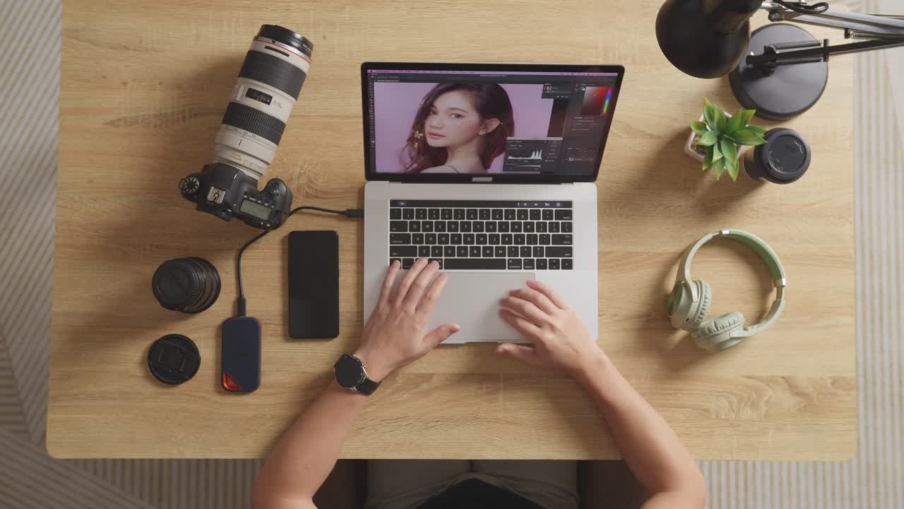 vista superior zoom en la toma de un editor masculino sentado en el espacio de trabajo usando una computadora portátil al lado de la cámara editando la foto de una mujer en casa