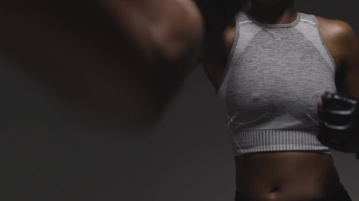 Primo piano in studio di una donna che indossa guantoni da boxe mentre fa sparring con un allenatore