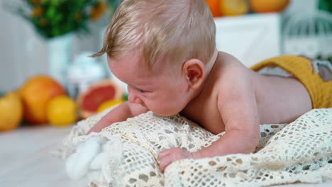 beautiful blond caucasian infant boy in yellow pants. blue-eyed baby struggling to raise head. close up. blurred backdrop.