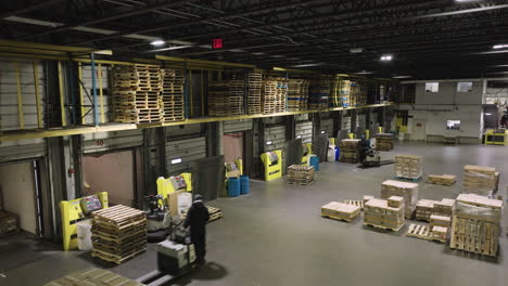 aerial high angle view of warehouse loading dock with workers operating forklifts and pallet jacks preparing shipments for trucks