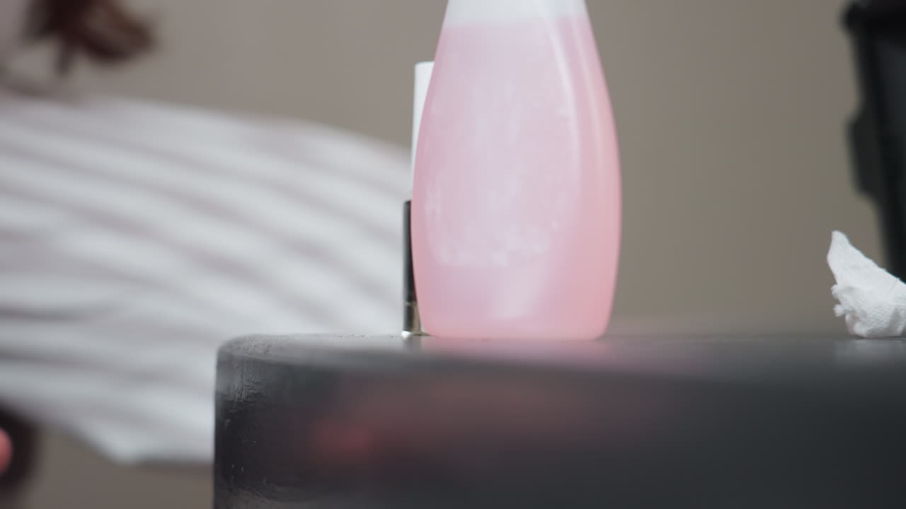Hand view shows demure hands covering black nail polish bottle beside pink remover, gentle twist to secure cap on table surface, soft indoor light, striped sleeve visible, calm, focused motion