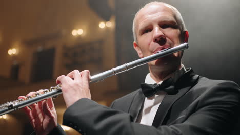 talented grey haired flutist is playing music by flute in opera house symphonic orchestra