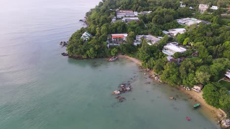 drone aerial slow parallax over tropical blue water with green mountainside houses