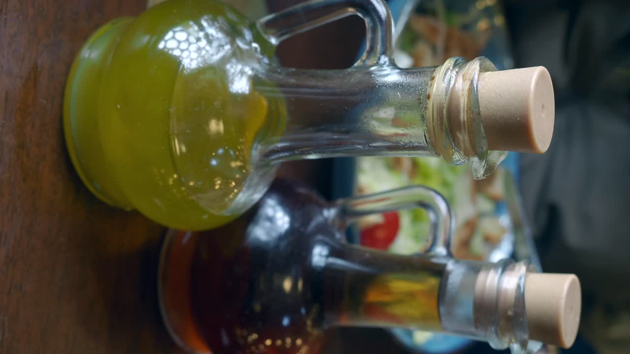 Olive oil and vinegar bottles on a dining table with a salad in the background