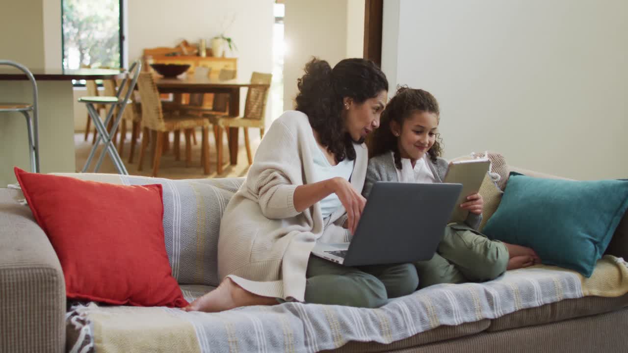 Happy mixed race mother and daughter sitting on the sofa,having fun and using laptop