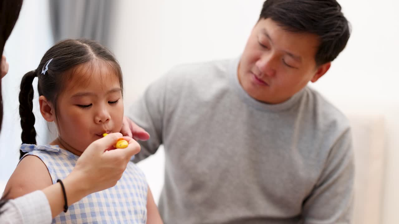 Father and daughter in bright living room, mother checks child’s temperature with digital thermometer