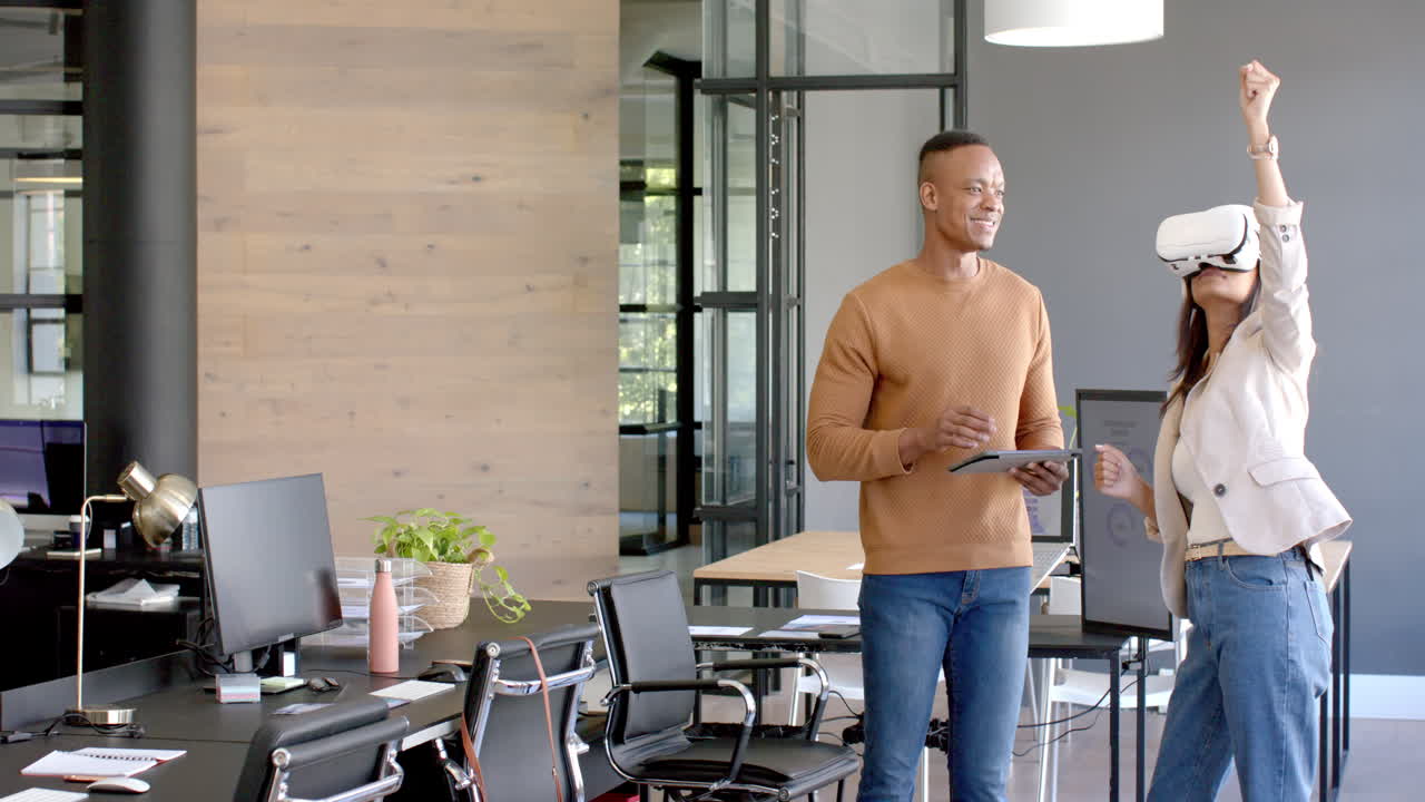 Using VR headset, woman interacting with colleague holding tablet in modern office, copy space