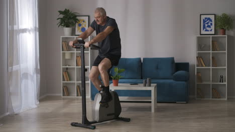 fitness at home middle-aged man is training on exercise bike in living room cardio workout healthy lifestyle