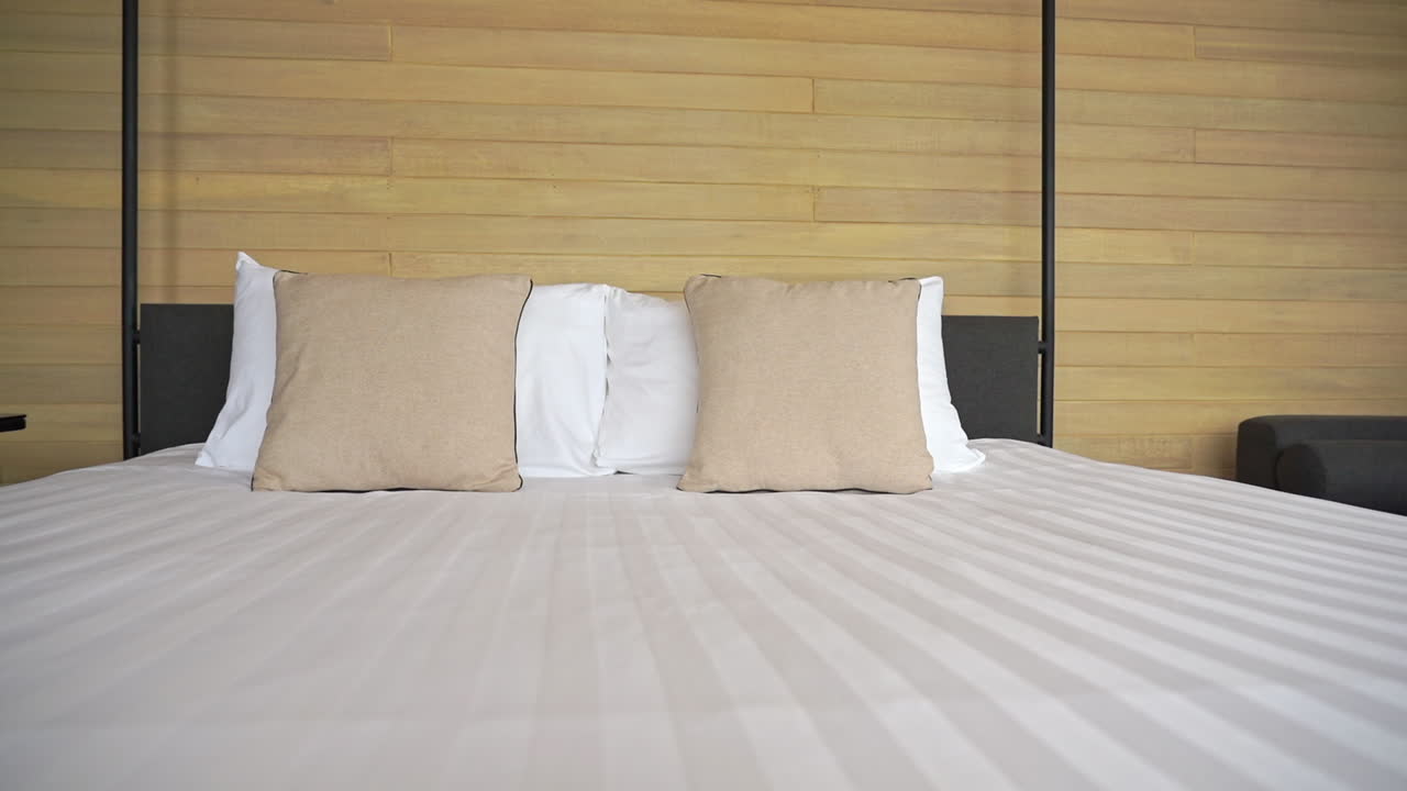 Luxury resort accommodations and soft bedding with modern interior design. Hotel bedroom. Bed with tan stripes and pillows to match wood plank wall. PAN LEFT