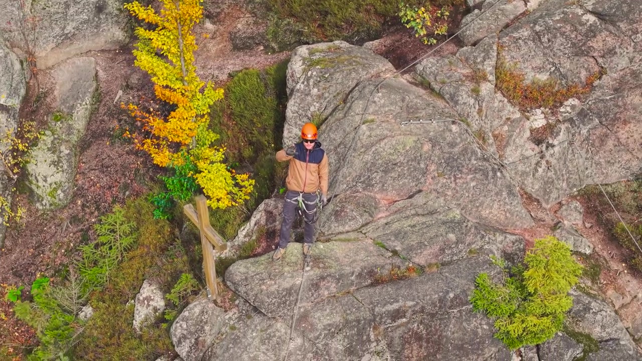 Aerial - rock climber stand on edge of steep cliff and wave hand, Czechia