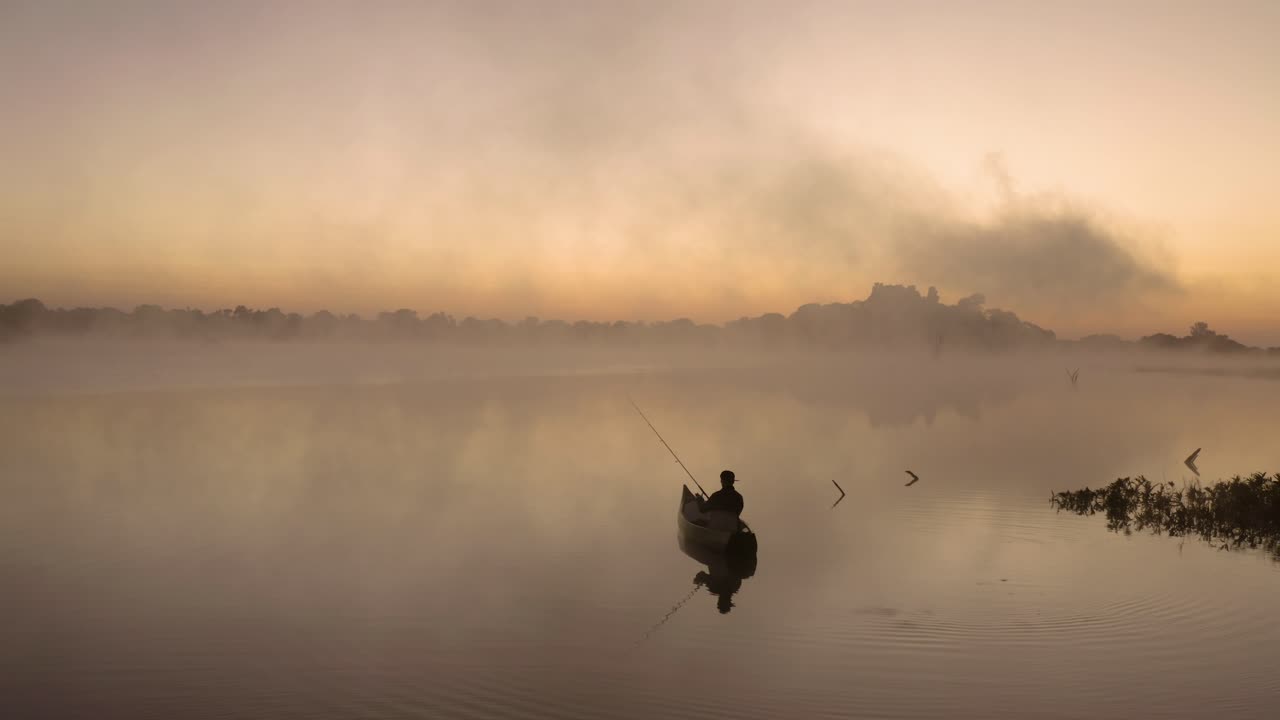 Pemandangan udara seorang pria yang sedang memancing sendirian di danau sebelum matahari terbit, Imire, Zimbabwe