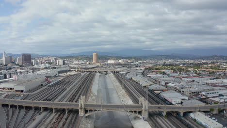 AERIAL:-Los-Angeles-River-with-Water-on-Cloudy-Overcast-Sky-next-to-Train-Tracks