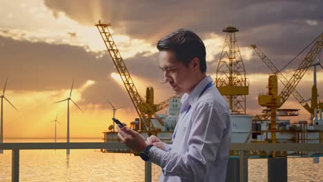 businessman using smartphone on oil rig platform with wind turbines sunset background