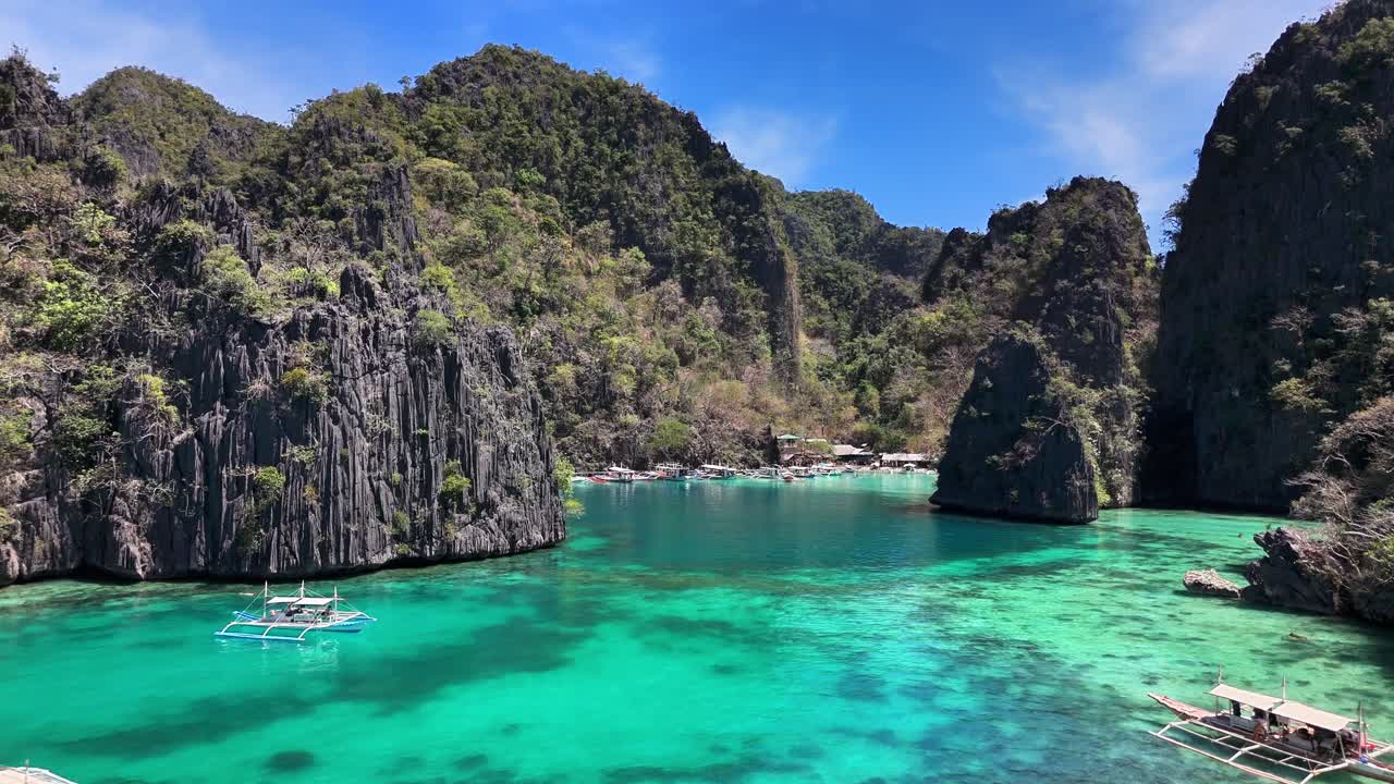 Turquoise waters and dramatic limestone cliffs surround Kayangan Jetty and Boardwalk in Coron, Philippines, with traditional outrigger boats floating in the calm, crystal-clear lagoon