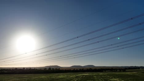 Drone-flying-past-powerlines-in-a-sunset-field