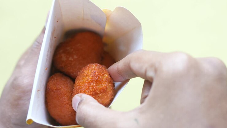 Mano che tiene un sacchetto di carta con crocchette di pollo fritte