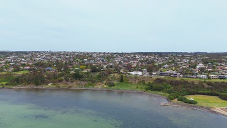 an expansive aerial view captures the residential landscape of point england, auckland, bordered by the calm waters of the sea, highlighting urban coastal living.