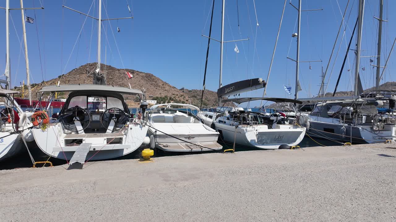 Greece,Patmos Island's town quay on a sunny day with blue skies.Boats stern to the town quay side by side, different countries flags are waiving at the back of the boats. quite day, no people around.