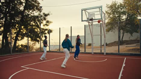 Three-blonde-girls-run-on-a-red-basketball-court-and-play-basketball-with-an-orange-basketball-ball-during-their-basketball-training-in-the-morning-in-the-summer