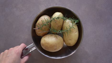 man put two fresh sprigs of rosemary on potatoes on pan