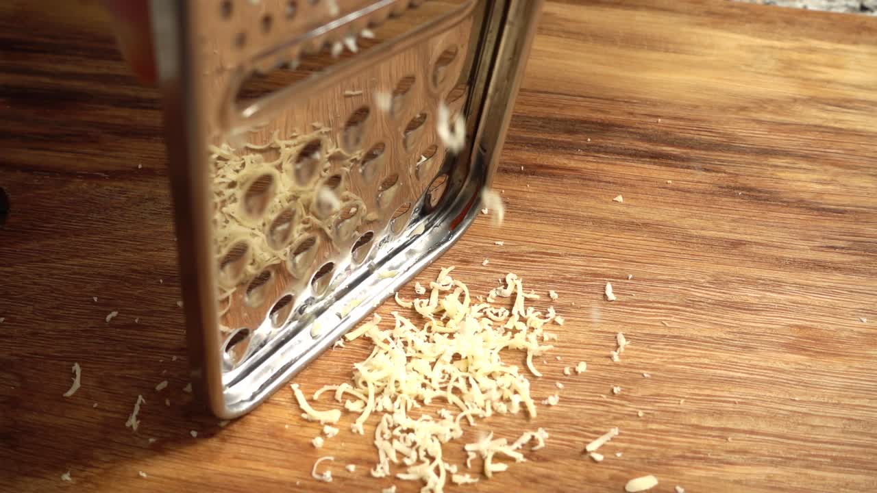 Der Koch reibt Käse auf einer Reibe. Zeitlupe.