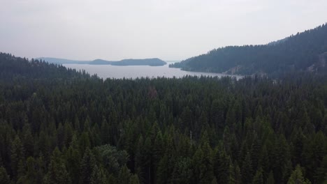 Drone-zoom-out-shot-of-Payette-Lake-from-the-dense,-green-forest-near-the-Payette-River-in-the-Idaho-wilderness