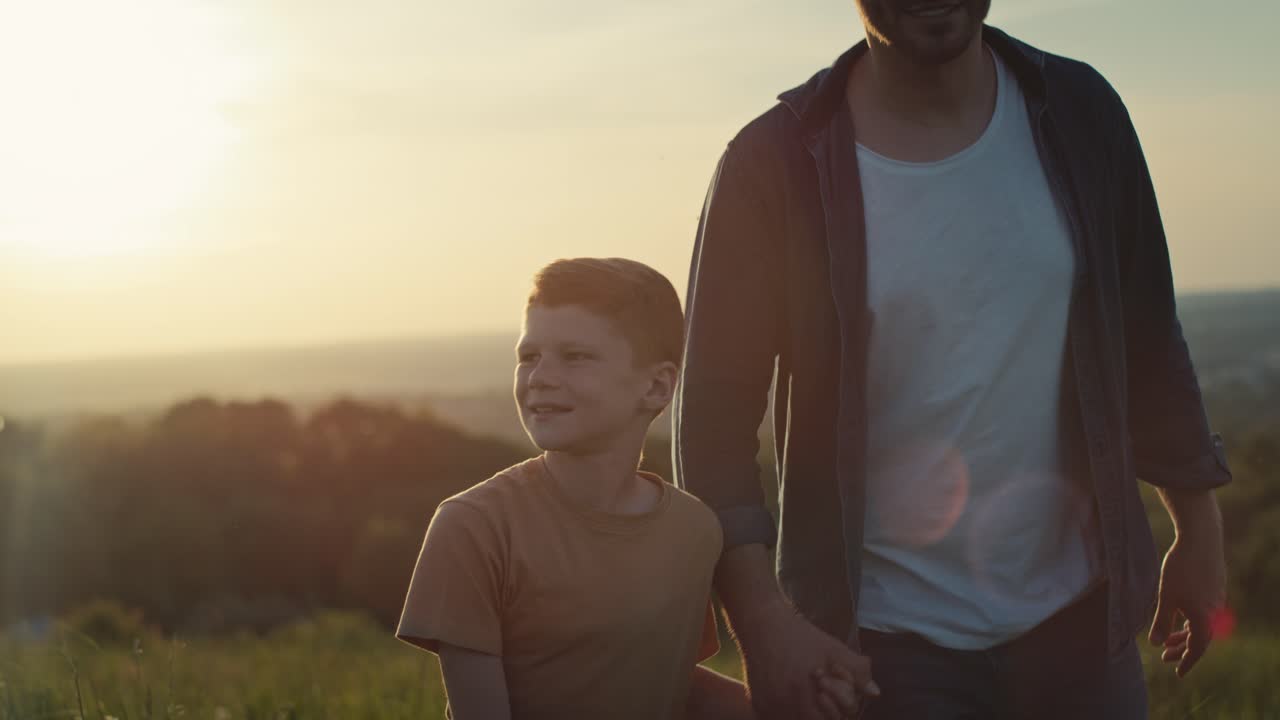 un niño caminando con su padre en el prado durante la puesta de sol.