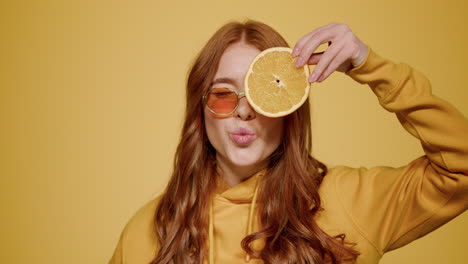 Linda-Chica-Sosteniendo-Rodajas-De-Naranja-En-El-Estudio.-Mujer-Mostrando-La-Lengua-Y-Guiñando-Un-Ojo